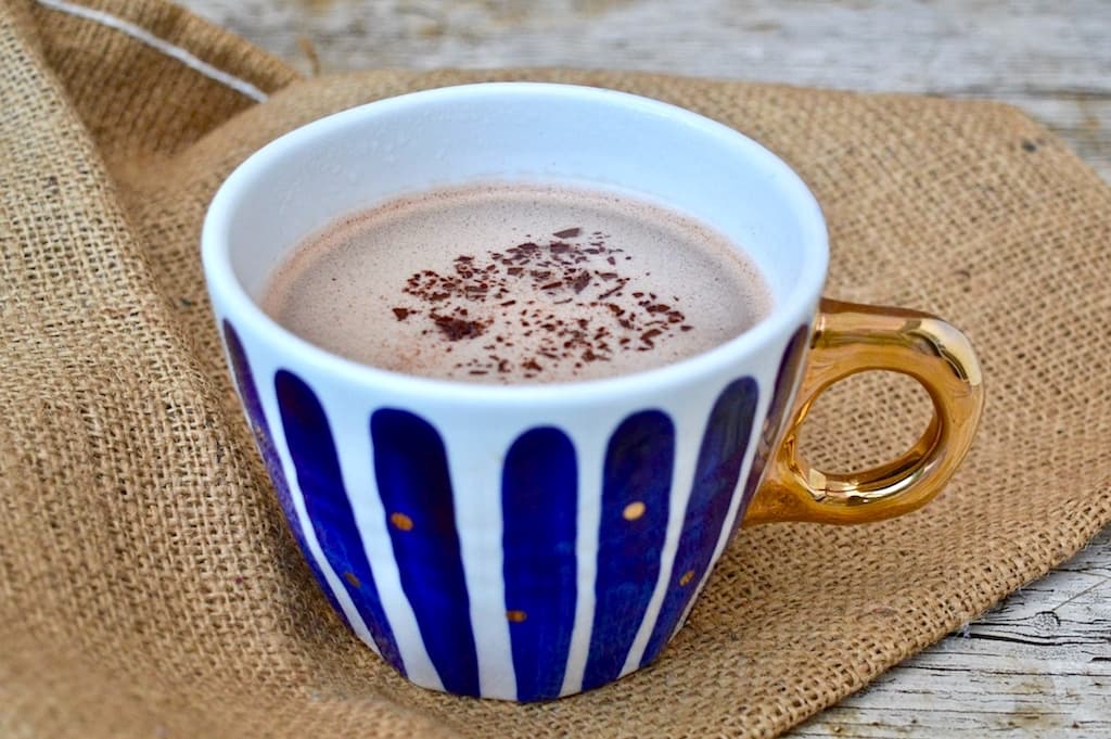 A blue stripy mug of gingerbread hot chocolate with chocolate sprinkles on top.