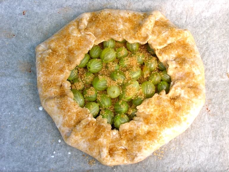 A raw French rustic tart filled with gooseberries and ready for the oven.
