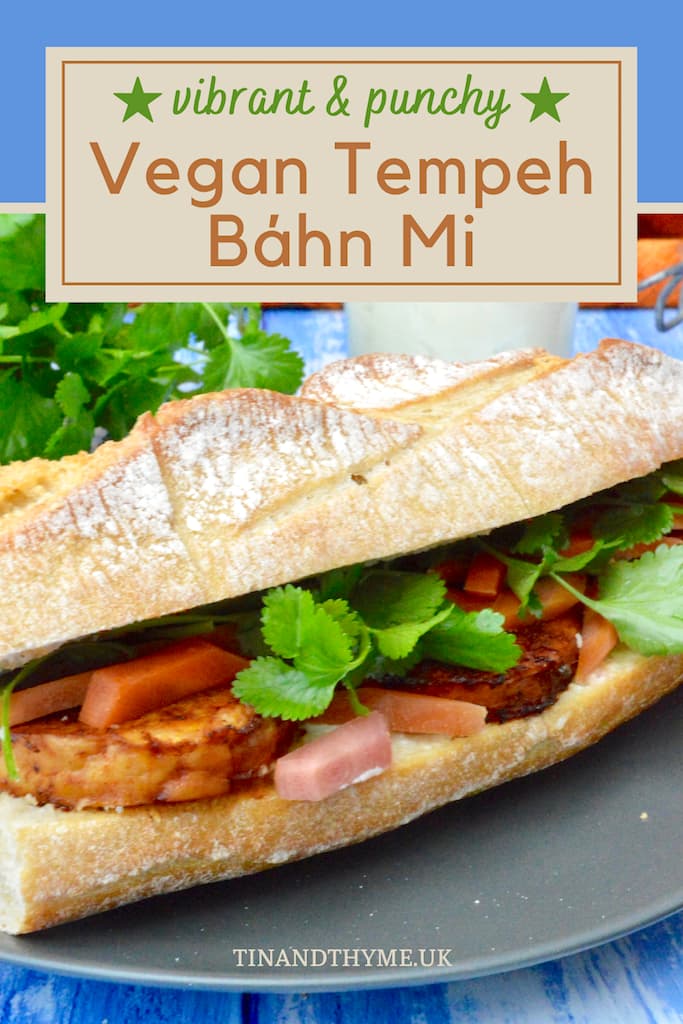 A close up of the middle section of a vegan tempeh bánh mi Vietnamese sandwich. A jar of mayonnaise and coriander (cilantro) leaves in the background.