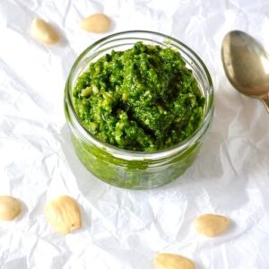 An open jar of wild garlic pesto with spoon and almonds scattered around.