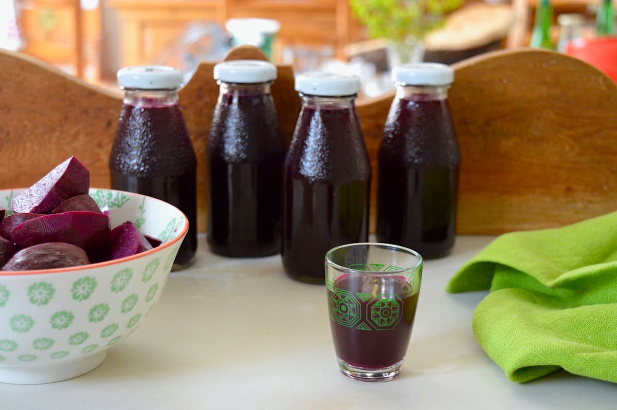 A glass of beet kvass with four bottles behind and a bowl of lacto-fermented beetroot.