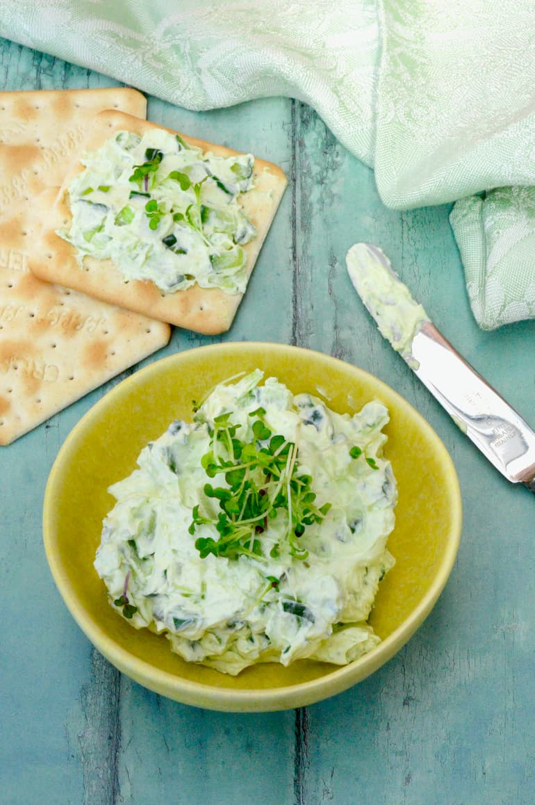 Cucumber cream cheese spread (or dip) in a yellow bowl with some spread on a cracker.