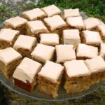 Squares of apple rose traybake with cream cheese icing on a glass platter.