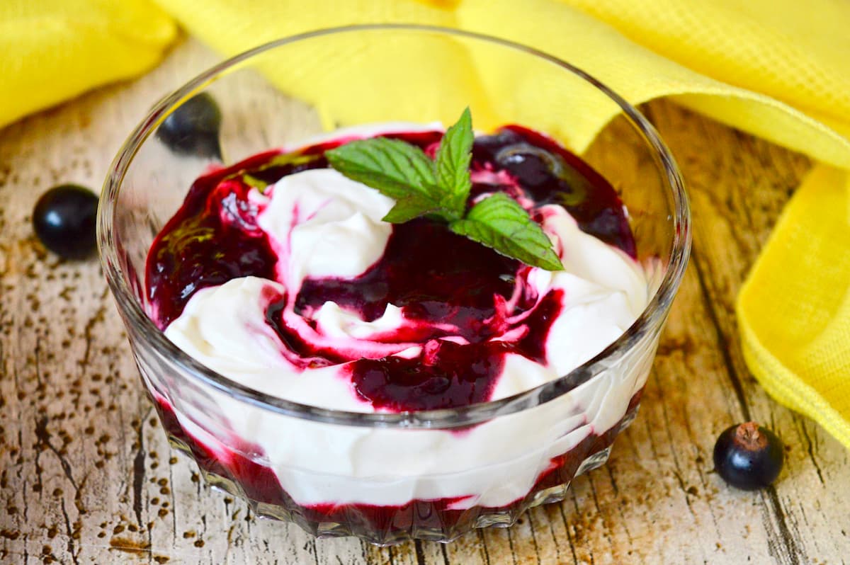 Glass dish containing swirled blackcurrant fool with a sprig of fresh mint.