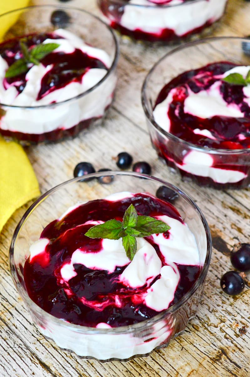 Four glass bowls of swirled blackcurrant fool with sprigs of fresh mint.