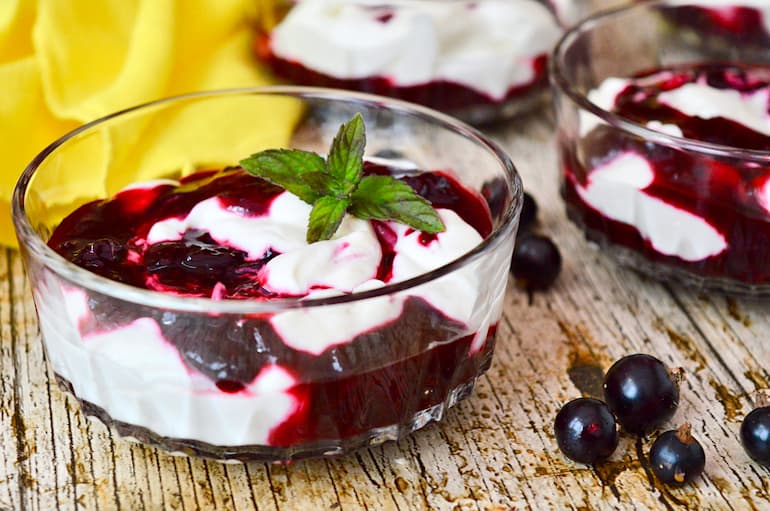 Glass dish containing swirled blackcurrant fool with a sprig of fresh mint.