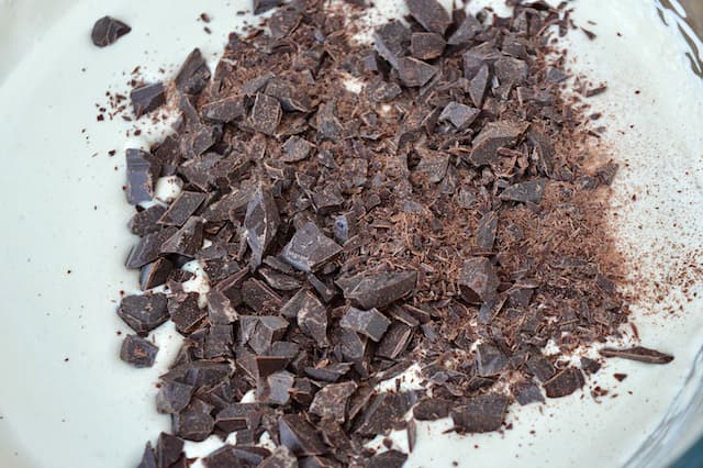 A bowl of whipped cream with a pile of chopped chocolate on the top.