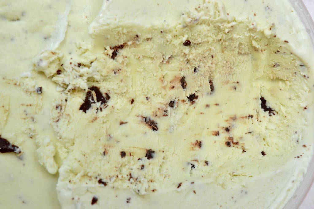 A tub of homemade mint chocolate chip ice cream with a few scoops removed.