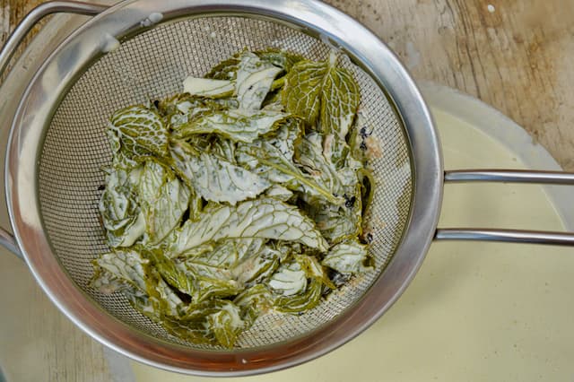 Steeped mint leaves draining through a sieve into a bowl.