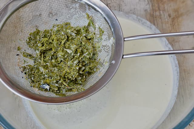 Steeped chopped mint leaves draining into a bowl through a sieve.