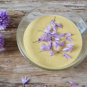 A bowl of tahini sauce with chive flowers scattered over the top.
