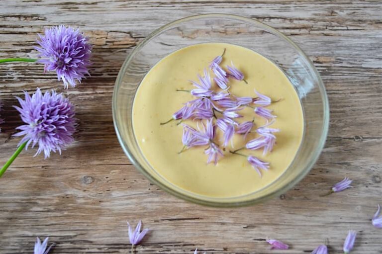 A bowl of tahini sauce with chive flowers scattered over the top.