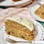 Slice of courgette cake with lime and mascarpone frosting with cake behind.