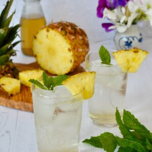 Two glasses of pineapple shrub diluted with ice and sparkling water.