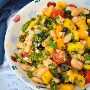 A bowl of Spanish white bean salad with blue cloth in background.
