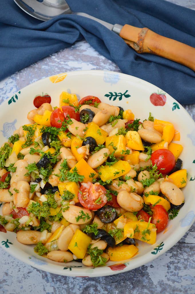 A bowl of Spanish white bean salad with spoon and navy cloth in background.