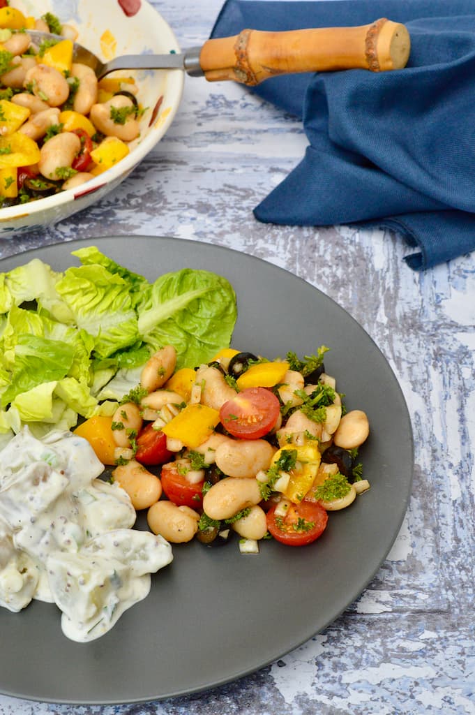 Butter bean salad on a grey plate with potato salad and lettuce leaves.