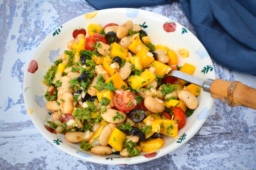 A bowl of Spanish white bean salad with spoon and navy cloth in background.