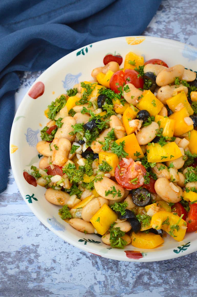 A bowl of Spanish white bean salad with blue cloth in background.
