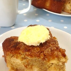 A slice of almond apple cider cake with a dollop of clotted cream on top.
