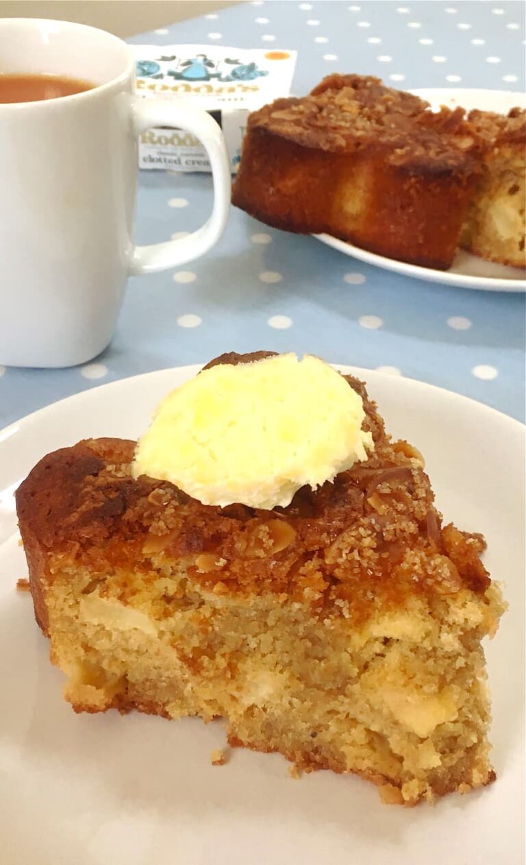 A slice of almond apple cider cake with a dollop of clotted cream on top.