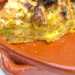 A slice of leftover cheese and leek bread pudding in a glazed terracotta dish.