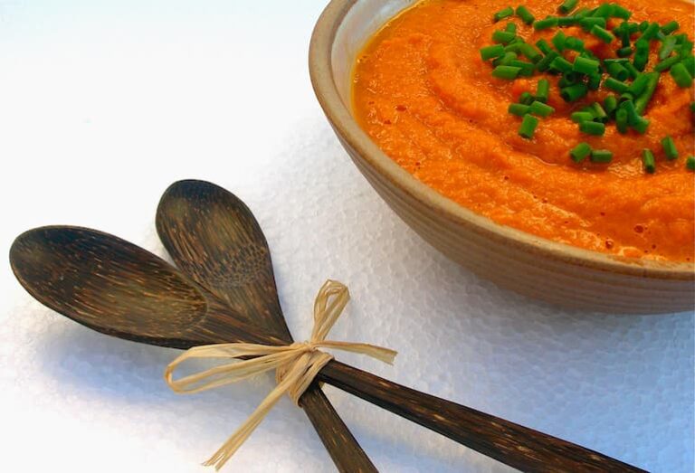 A bowl of raw tomato sauce with tinned tomatoes and seaweed. Chopped chives adorns the top and a pair of wooden spoons on the side.