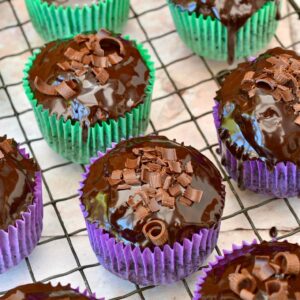 Glossy chocolate covered vegan courgette cupcakes in green and purple paper cases.