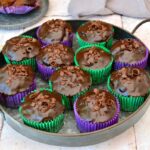 A tray of vegan chocolate courgette cupcakes in green and purple cases.