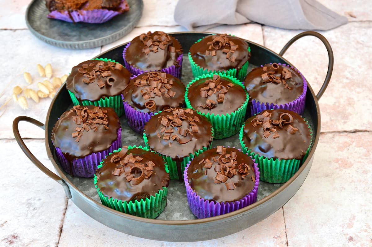 A tray of vegan chocolate courgette cupcakes in green and purple cases.