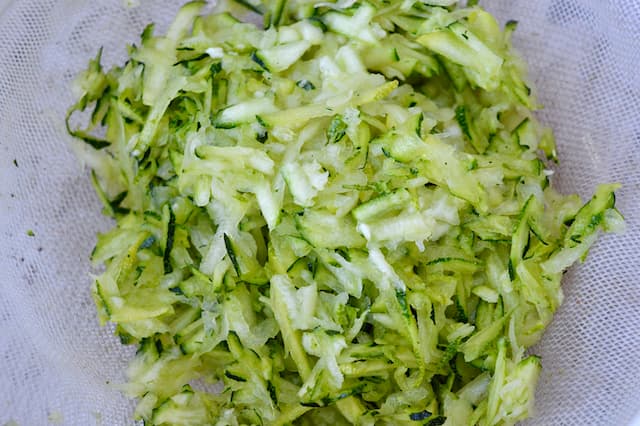 Grated courgette draining in a sieve.