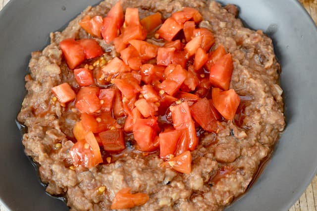 Diced tomatoes on top of a bowl of mashed fava beans.