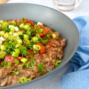A bowl of ful medames (Egyptian fava bean stew) with chopped tomato, parsley and spring onions on top.