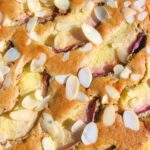 Close up of the top of a peach and white chocolate cake scattered with flaked almonds.