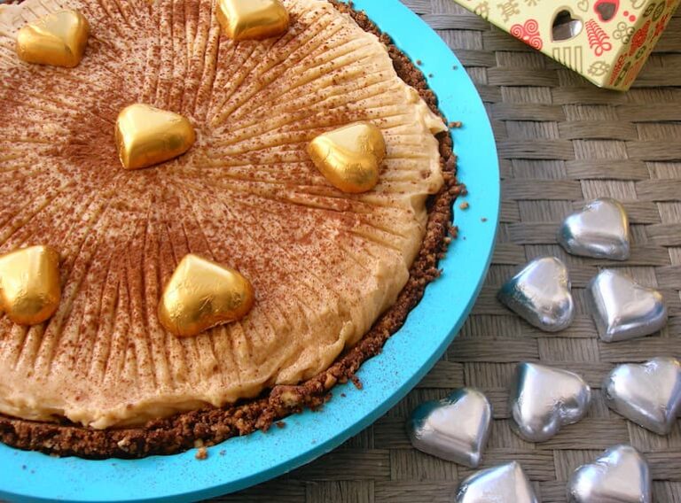 A no-bake chocolate cashew pie decorated with gold hearts in a turquoise silicone flan dish.