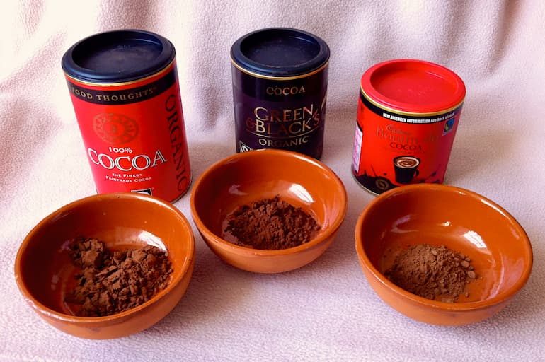 Three pots of cocoa powder and three dishes of the cocoa from each pot.