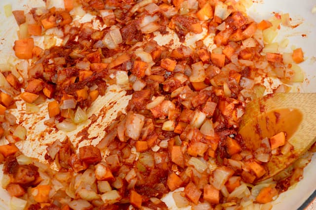 Diced carrots, onions and tomato purée frying in a ceramic pan.