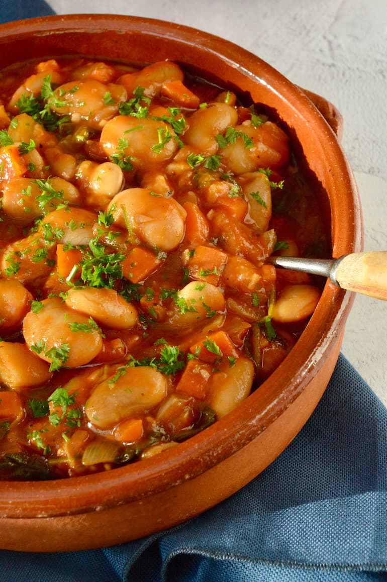 A ceramic dish filled with Greek butter beans in tomato sauce and parsley scattered over the top.