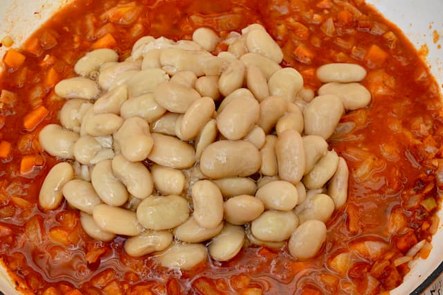 Jarred butter beans in a pan of tomato sauce.