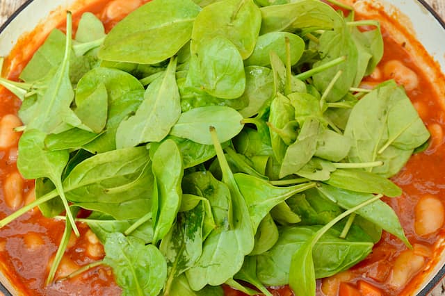 Pile of baby leaf spinach on top of a pan of Greek gigantes.