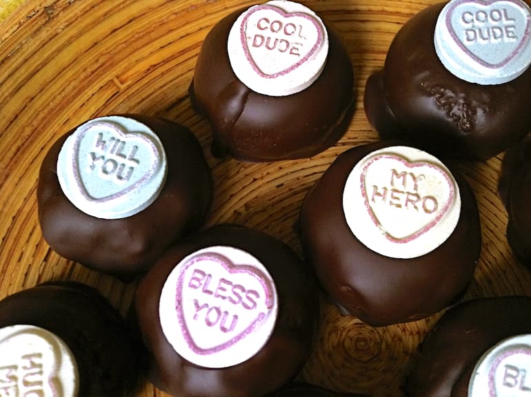 Close up of five chocolate hazelnut cake truffles topped with love hearts.