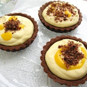 Three lime curd and mascarpone chocolate tarts on a glass platter.