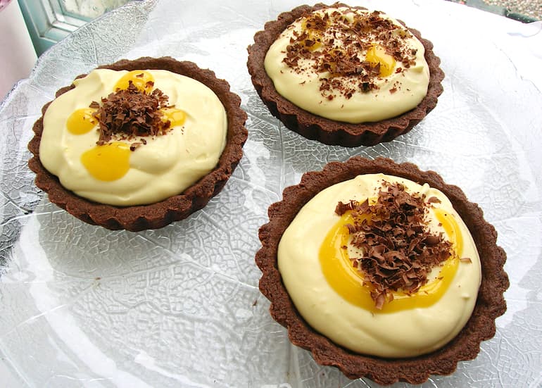 Three lime curd and mascarpone chocolate tarts on a glass platter.