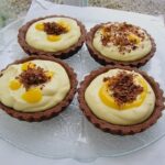 Four lime curd and mascarpone chocolate tarts on a glass platter.