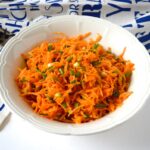 Grated carrot salad with chives in a cream serving bowl.
