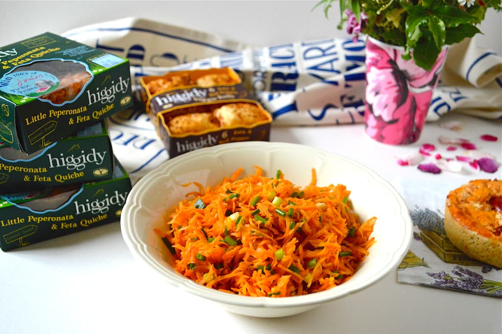 Grated carrot salad in a cream bowl, with various Higgidy pies in the background.