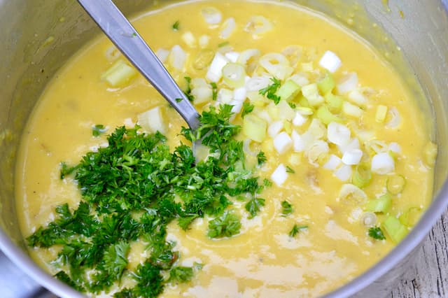 A pan of whisked eggs with a fork and chopped parsley and scallions on the top.