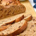 Three slices of wholemeal prune and walnut fruit loaf on a board with main loaf and butter dish.
