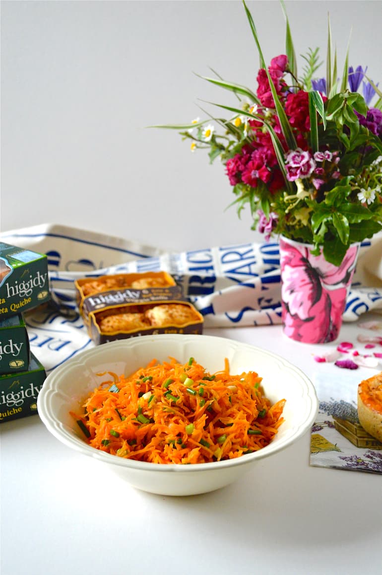 Grated carrot salad in a cream bowl, with various Higgidy pies in the background.