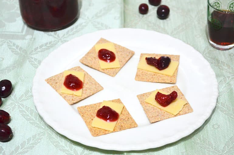 A plate of crackers with cheese slices topped with homemade cranberry sauce.